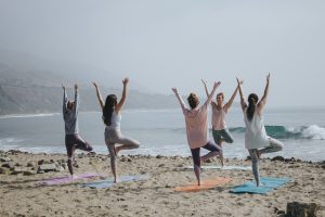 A group of five women practise the tree pose in yoga on the beach 